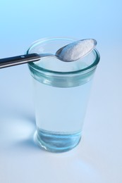 Glass of water and spoon with baking soda on light blue background