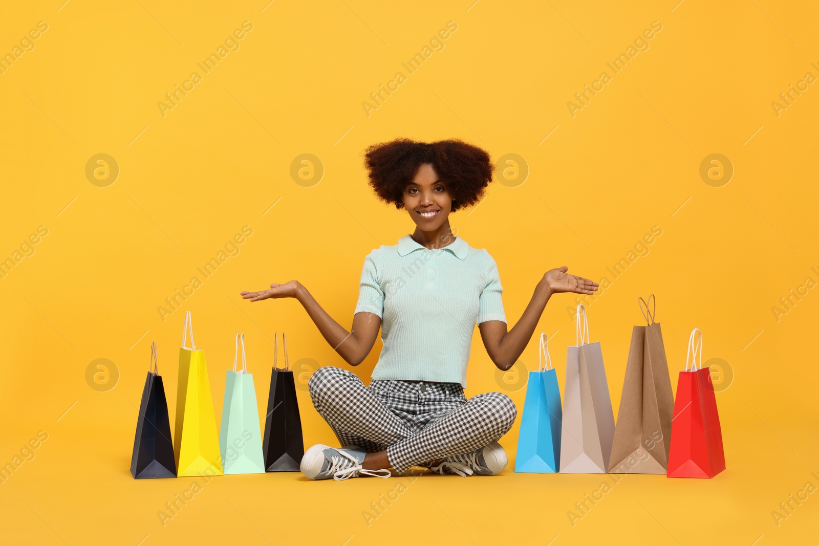 Photo of Happy African American woman with shopping bags on orange background