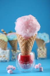 Photo of Sweet cotton candy in waffle cone and marshmallows on light blue background, closeup