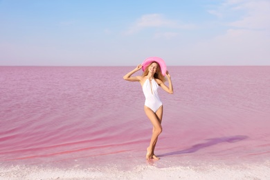 Beautiful woman in swimsuit posing near pink lake on sunny day