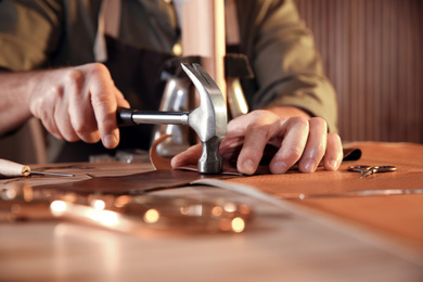 Photo of Man working with piece of leather at table, closeup