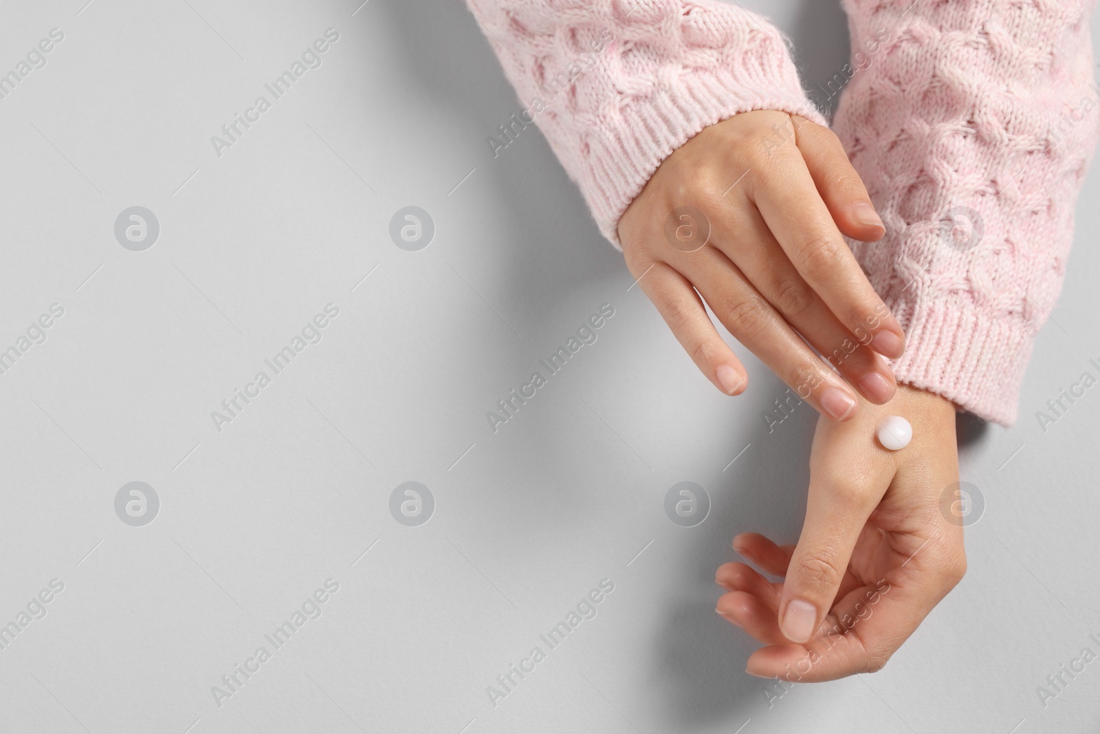 Photo of Woman applying cosmetic cream onto hand on light grey background, top view. Space for text