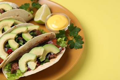 Photo of Delicious tacos with meat, vegetables and avocado served on yellow table, closeup