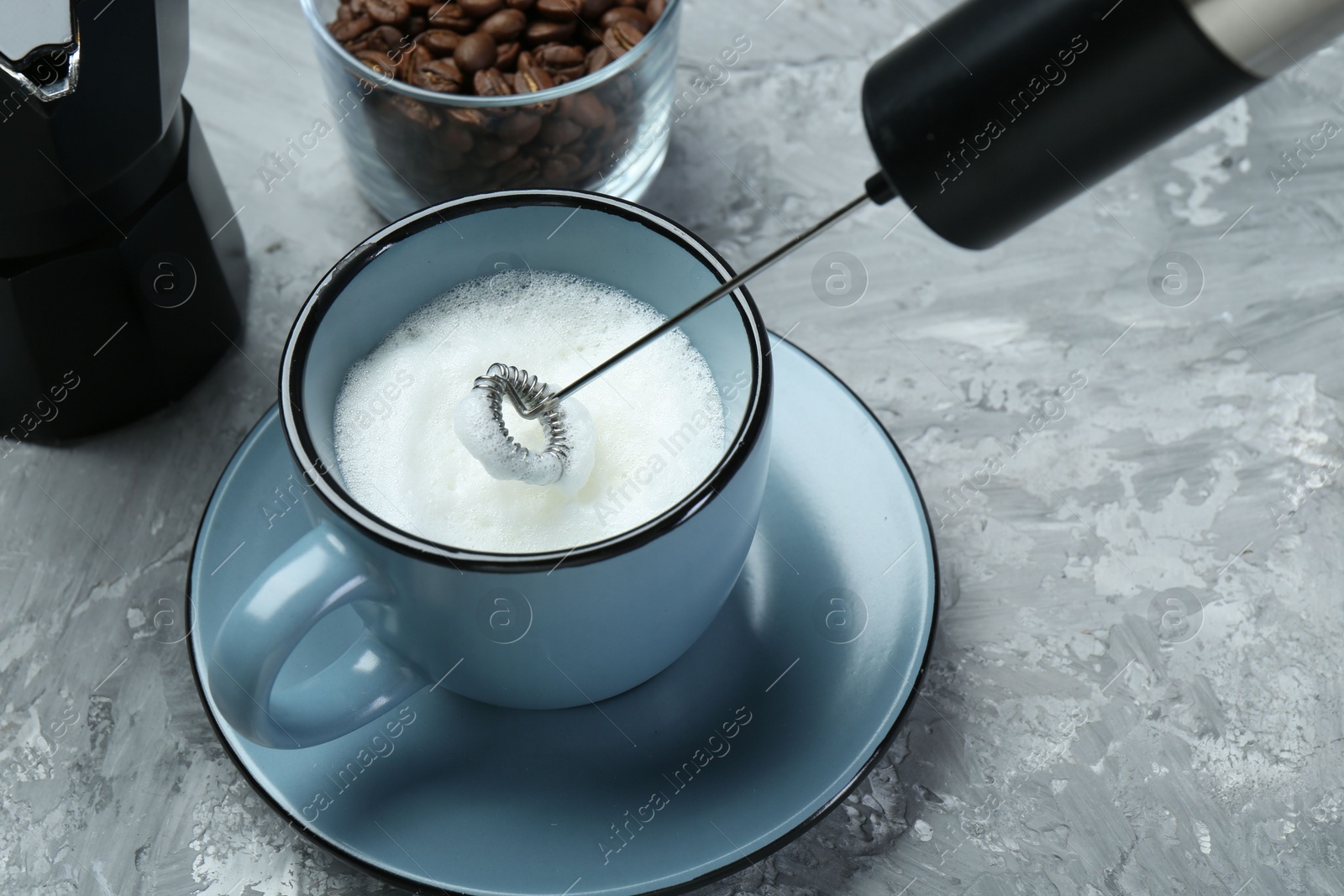 Photo of Whisking milk in cup with mini mixer (milk frother) on grey textured table, closeup