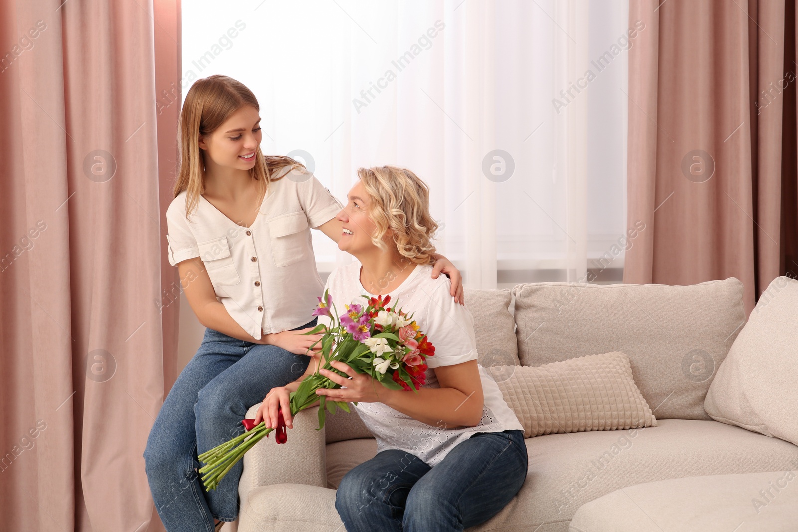 Photo of Young daughter congratulating her mom with flowers at home. Happy Mother's Day