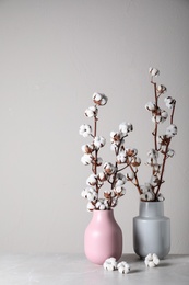 Beautiful cotton flowers in vases on stone table against grey background, space for text