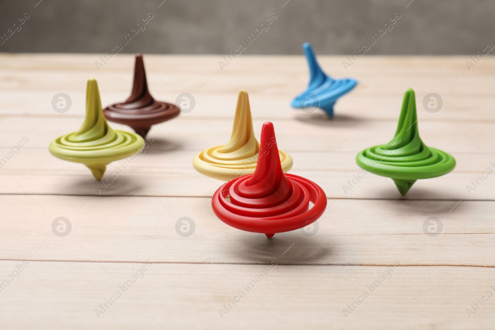 Photo of Bright spinning tops on light wooden table, closeup