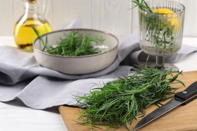 Photo of Fresh tarragon sprigs and knife on white wooden table, closeup