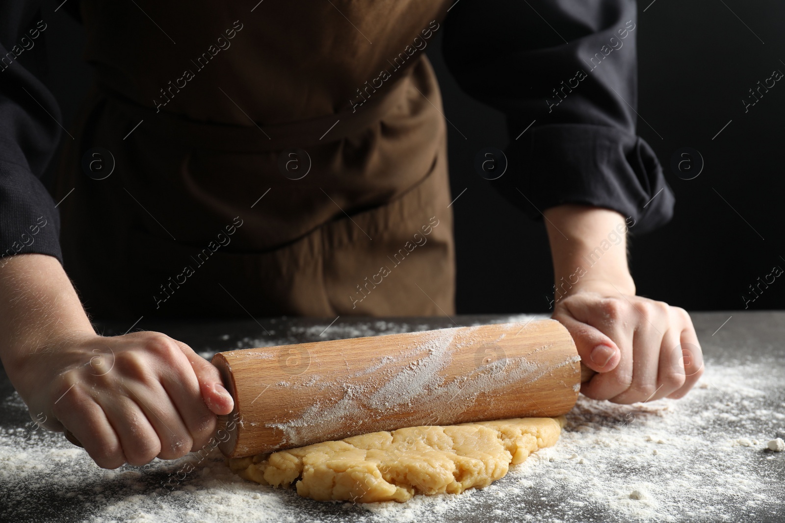 Photo of Making shortcrust pastry. Woman rolling raw dough at table, closeup