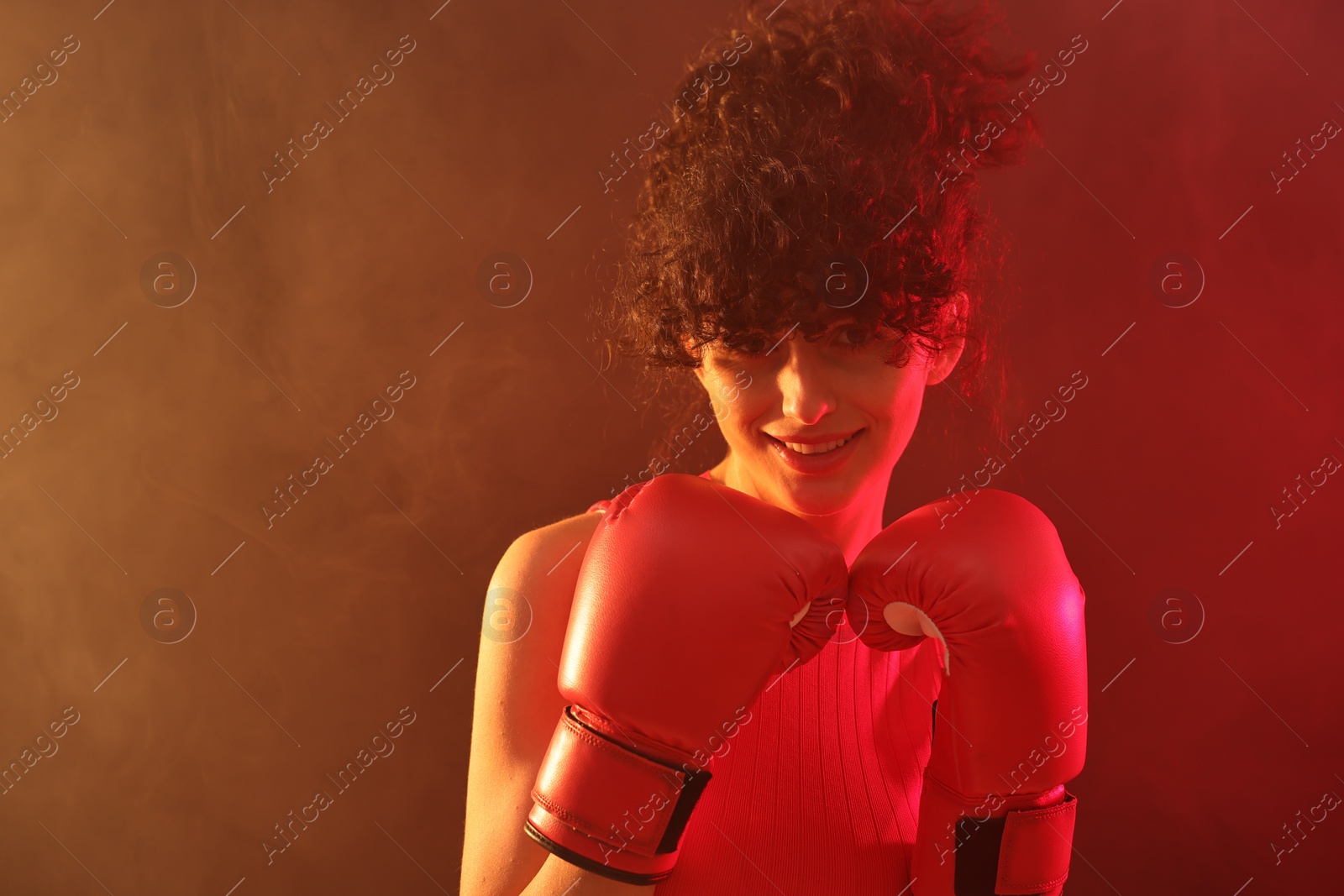 Photo of Beautiful young woman with boxing gloves on color background in neon lights and smoke. Space for text