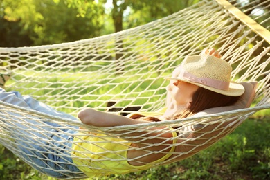 Young woman with hat resting in comfortable hammock at green garden