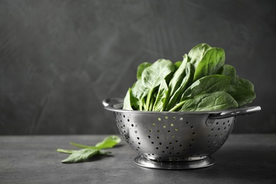 Colander with fresh green healthy spinach on grey table, space for text