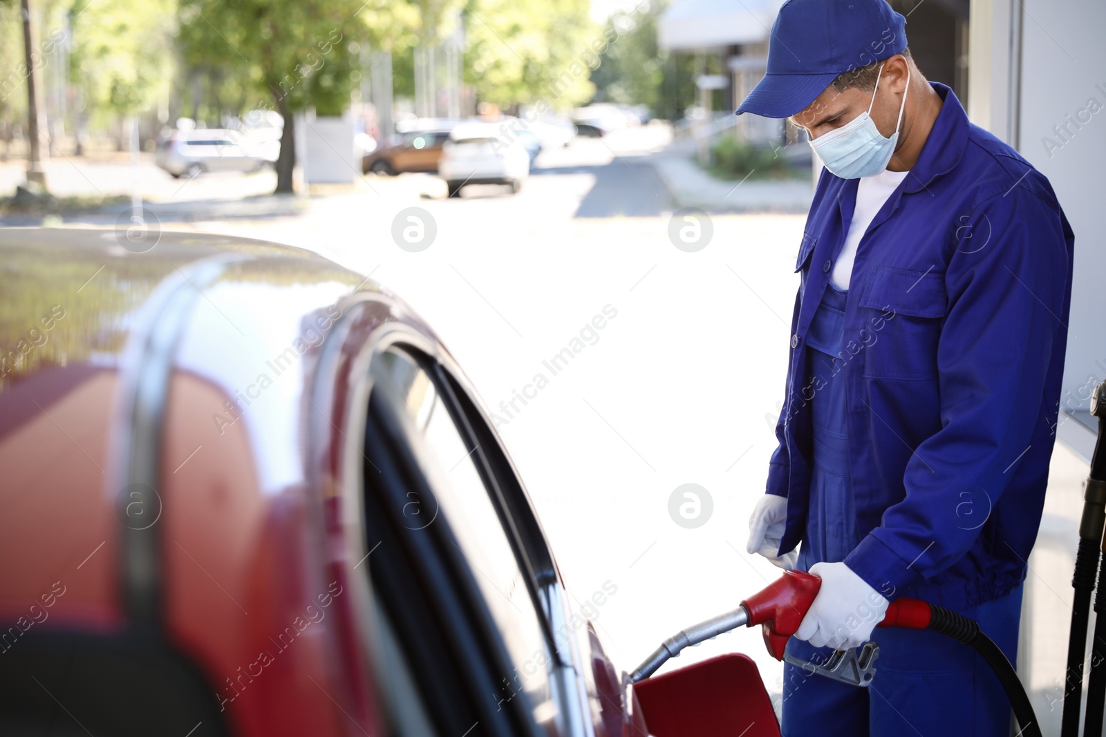 Photo of Worker in mask refueling car at modern gas station