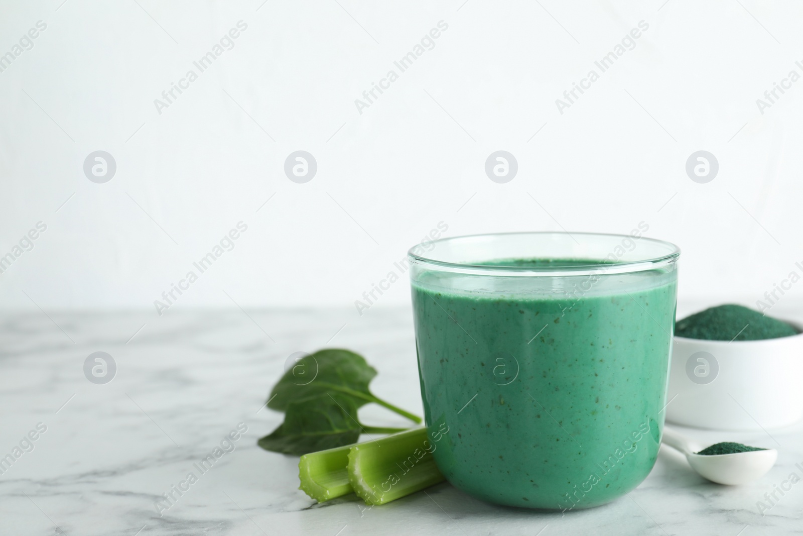 Photo of Glass of spirulina smoothie, powder and celery on table against white background. Space for text