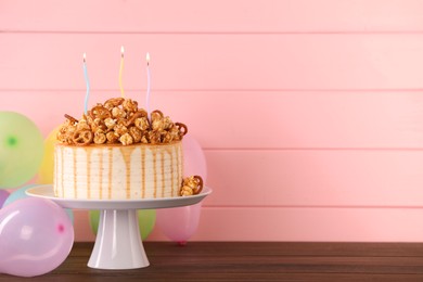 Photo of Caramel drip cake decorated with popcorn and pretzels near balloons on wooden table, space for text