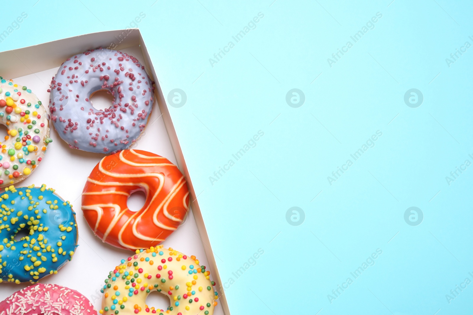 Photo of Delicious glazed donuts on light blue background, top view. Space for text