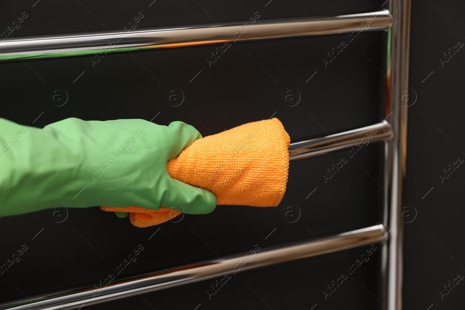 Photo of Woman cleaning heated towel rail with rag, closeup