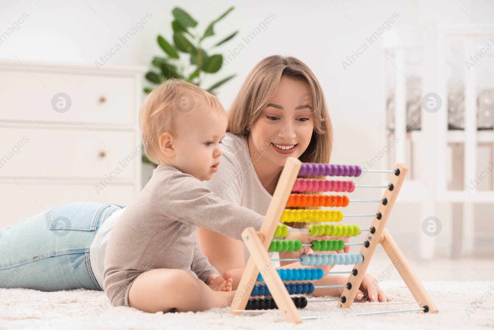 Photo of Children toys. Happy mother and her little son playing with wooden abacus on rug at home