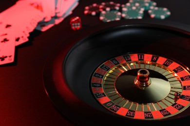 Photo of Roulette wheel with ball, chips, dice and playing cards on dark table, closeup. Casino game