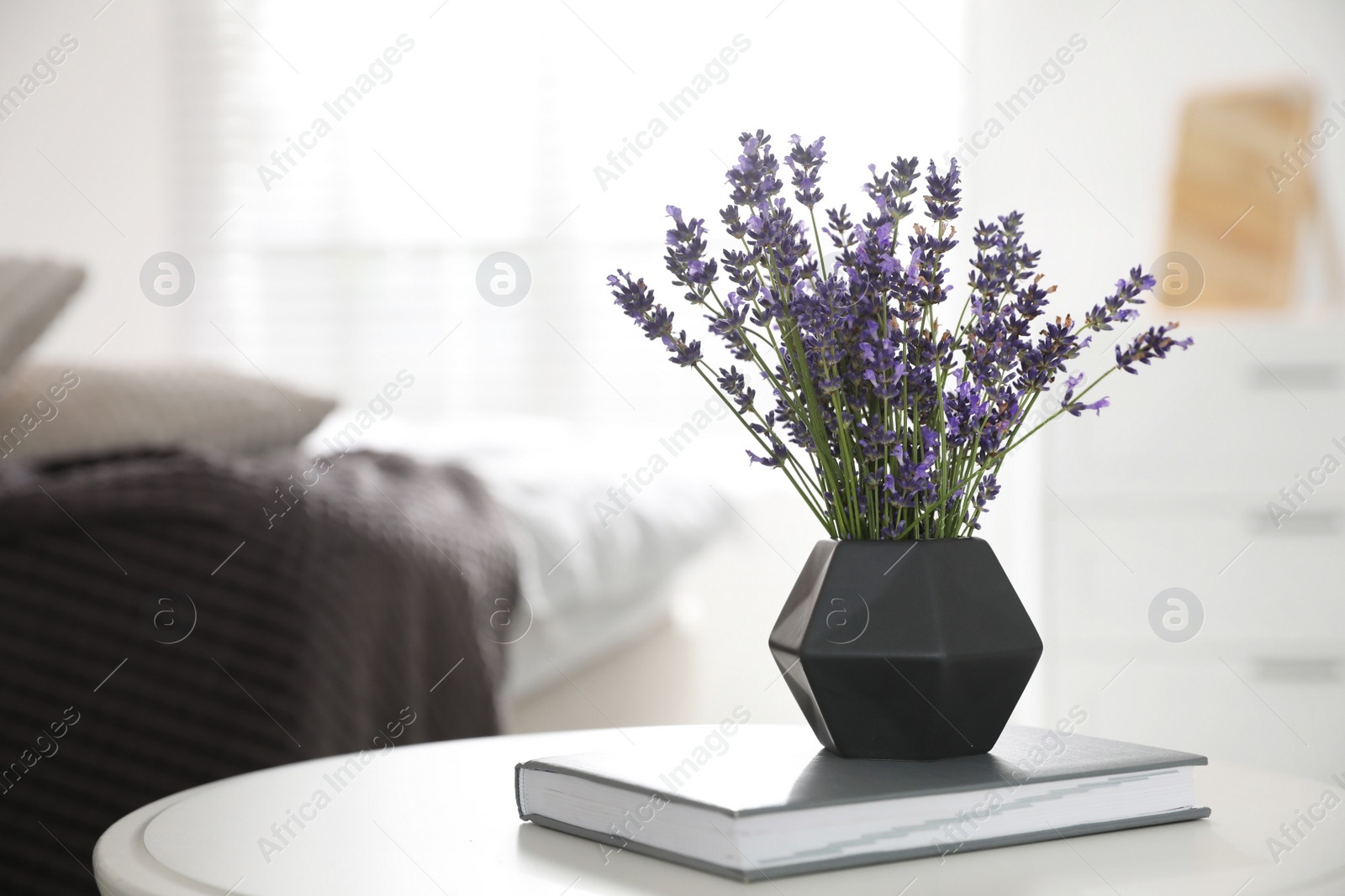 Photo of Beautiful lavender flowers and book on white table indoors. Space for text