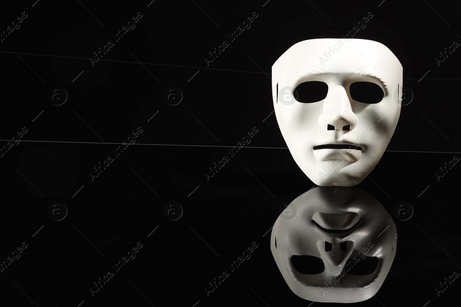 Photo of Plastic face mask on black mirror surface, space for text. Theatrical performance