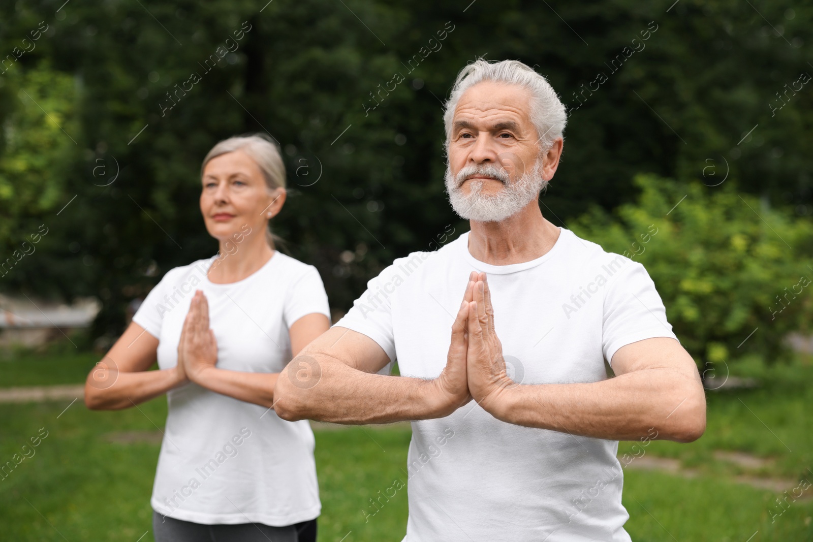 Photo of Senior couple practicing yoga in park, selective focus