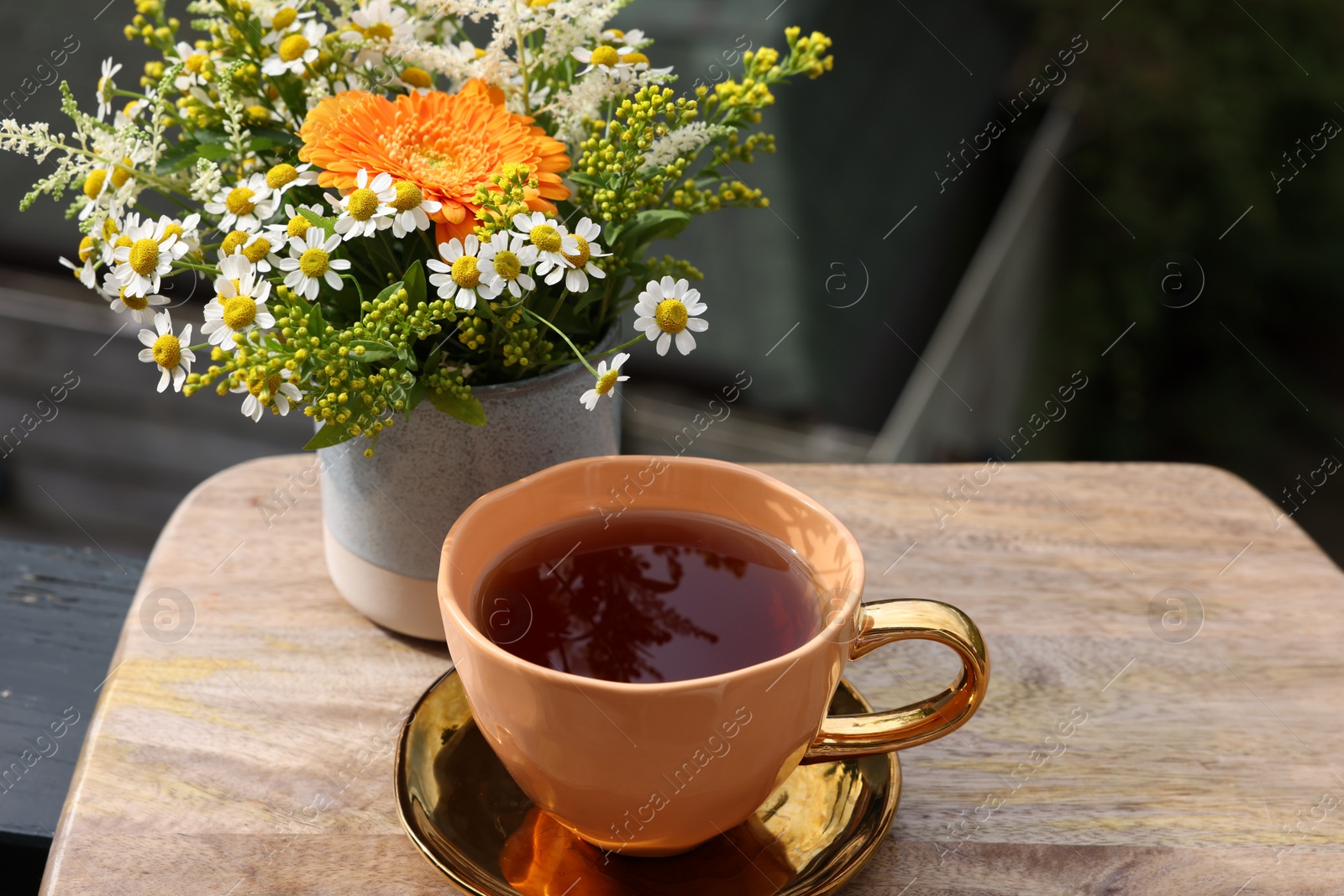 Photo of Cup of delicious chamomile tea and fresh flowers outdoors on sunny day