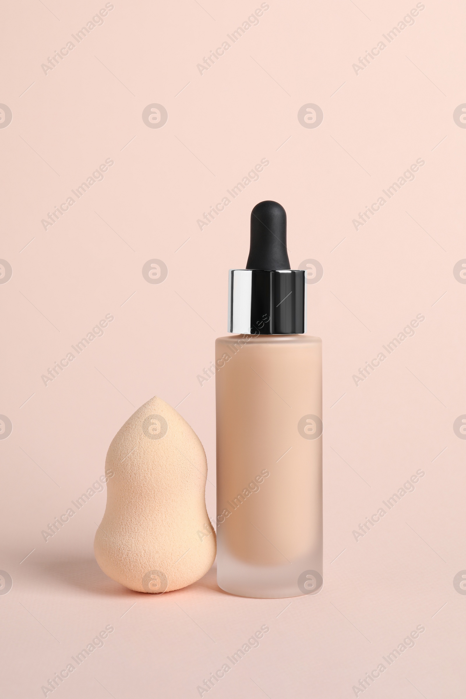 Photo of Bottle of skin foundation and sponge on beige background. Makeup product