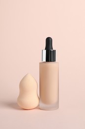 Bottle of skin foundation and sponge on beige background. Makeup product