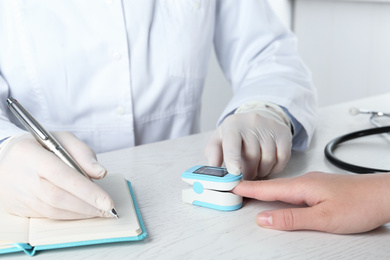 Doctor examining patient with fingertip pulse oximeter at white wooden table, closeup