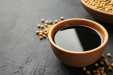 Photo of Tasty soy sauce in bowl and soybeans on black table, closeup. Space for text