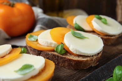 Delicious sandwiches with mozzarella, yellow tomatoes and basil on wooden board