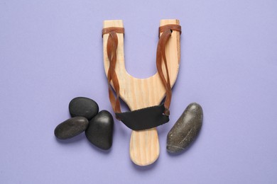 Wooden slingshot with stones on violet background, flat lay