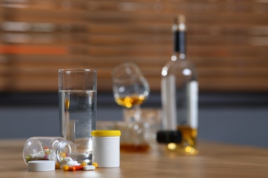 Photo of Glass of water, pills and alcohol on table indoors, space for text. Hangover remedy