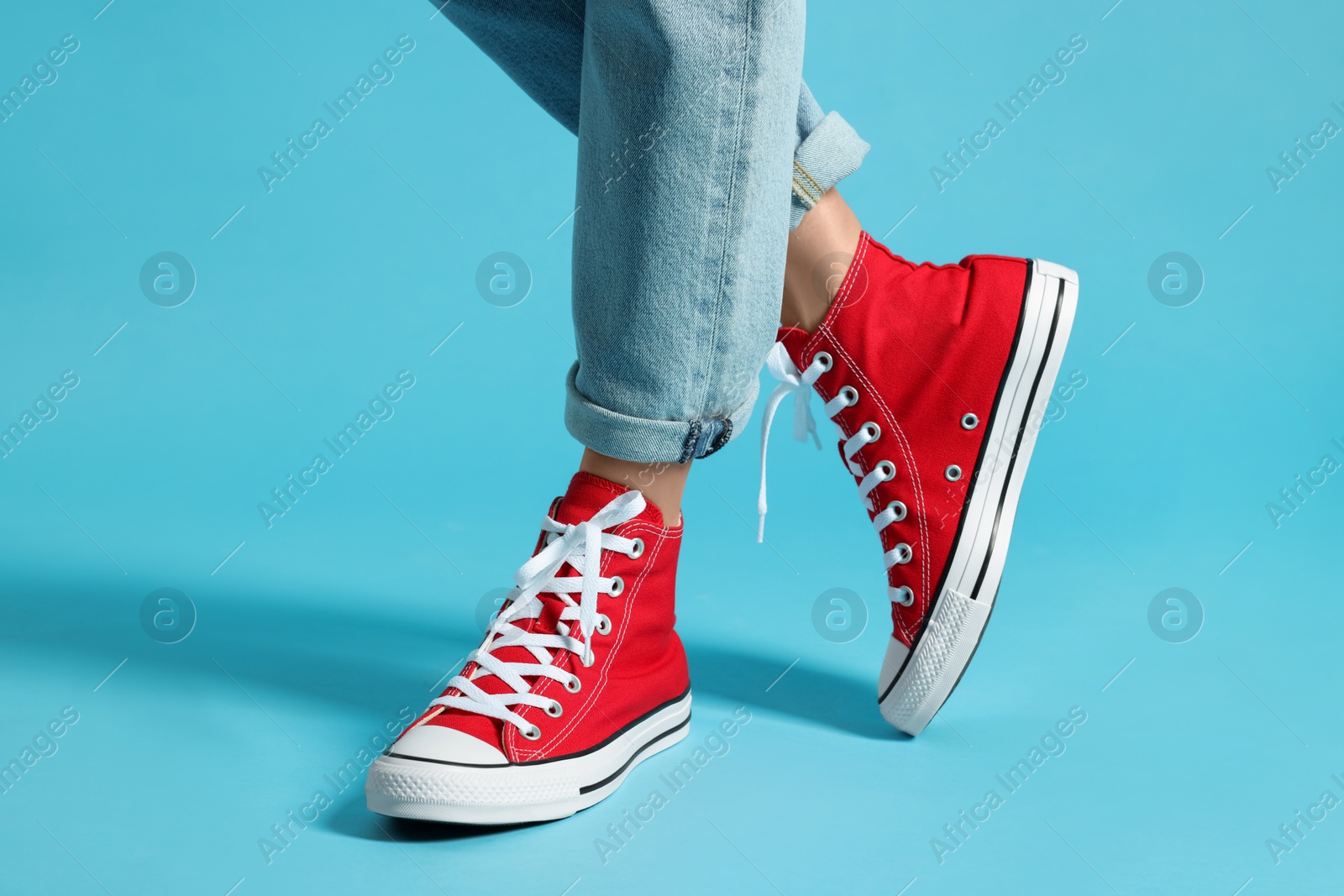 Photo of Woman in stylish gumshoes on light blue background, closeup