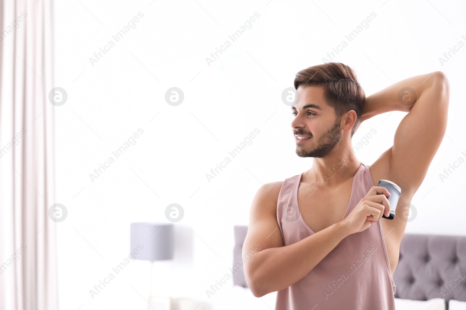 Photo of Handsome young man applying deodorant in bedroom. Space for text