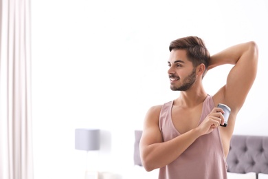 Handsome young man applying deodorant in bedroom. Space for text