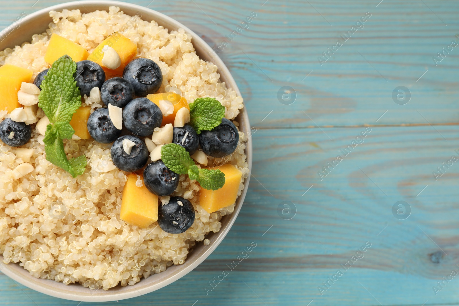 Photo of Tasty quinoa porridge with blueberries, pumpkin and mint in bowl on light blue wooden table, top view. Space for text