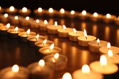 Burning candles on wooden table in darkness, closeup