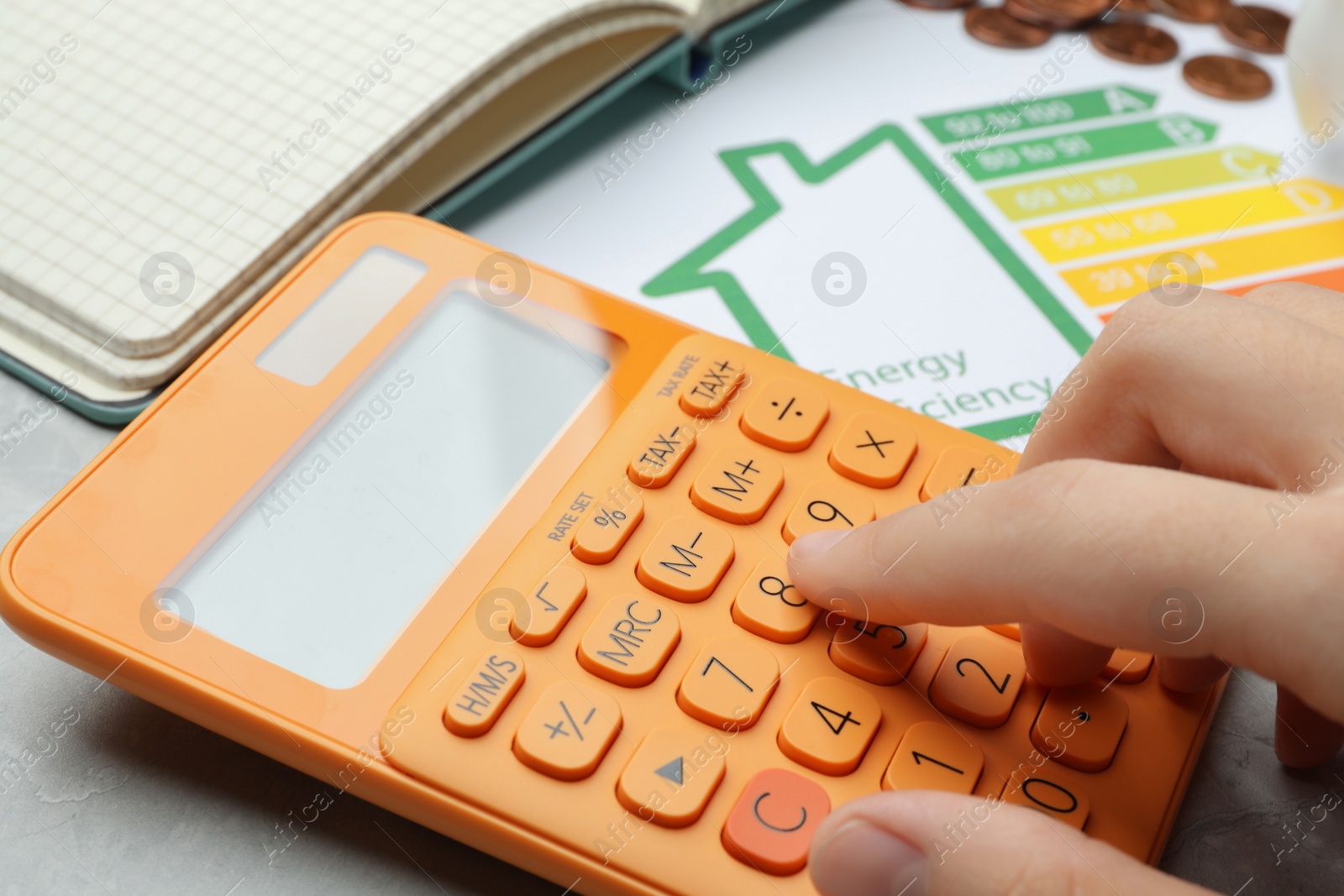 Photo of Woman with calculator and energy efficiency rating chart at table, closeup