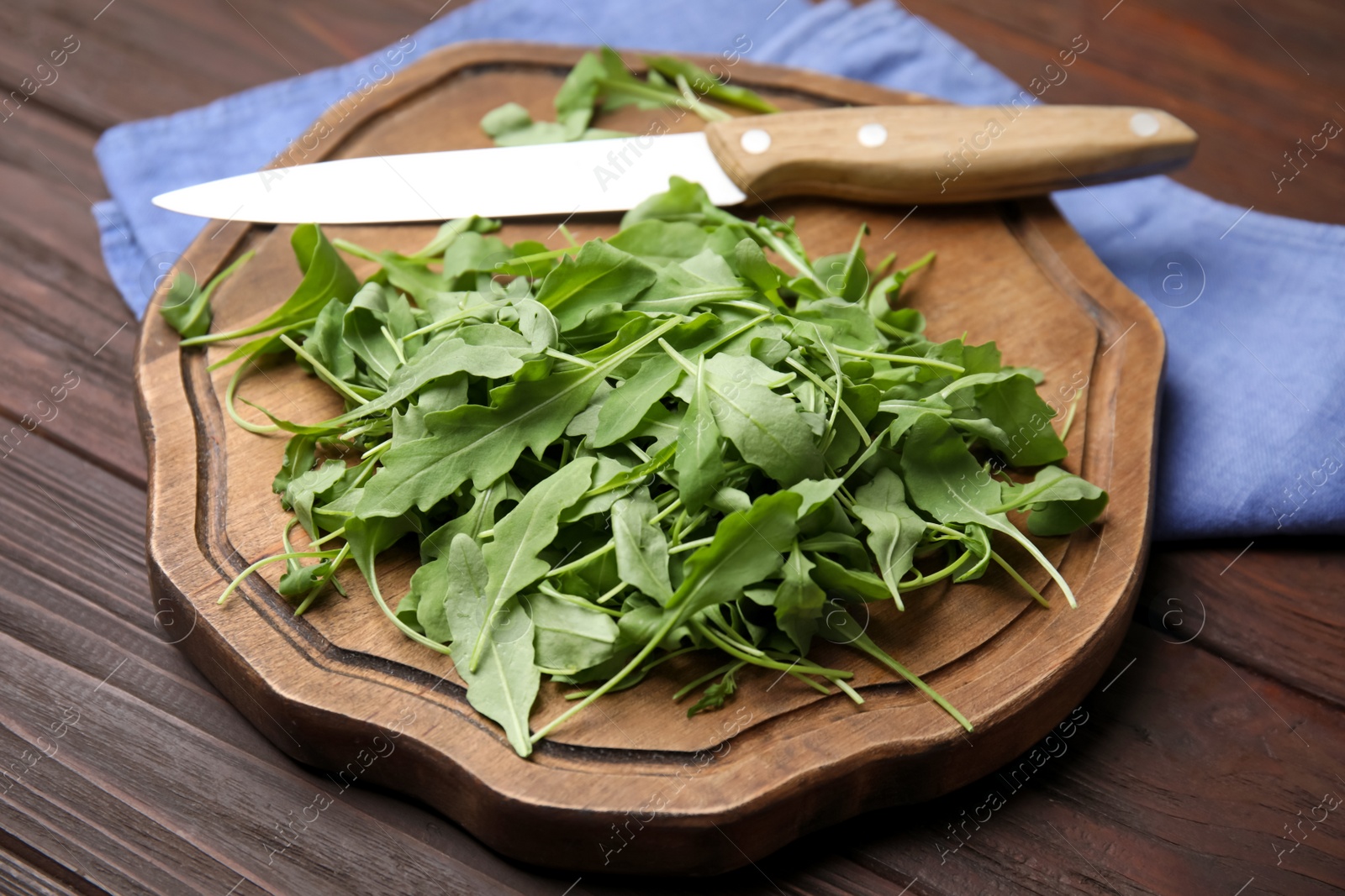 Photo of Cutting board with fresh arugula leaves and knife on wooden table, closeup