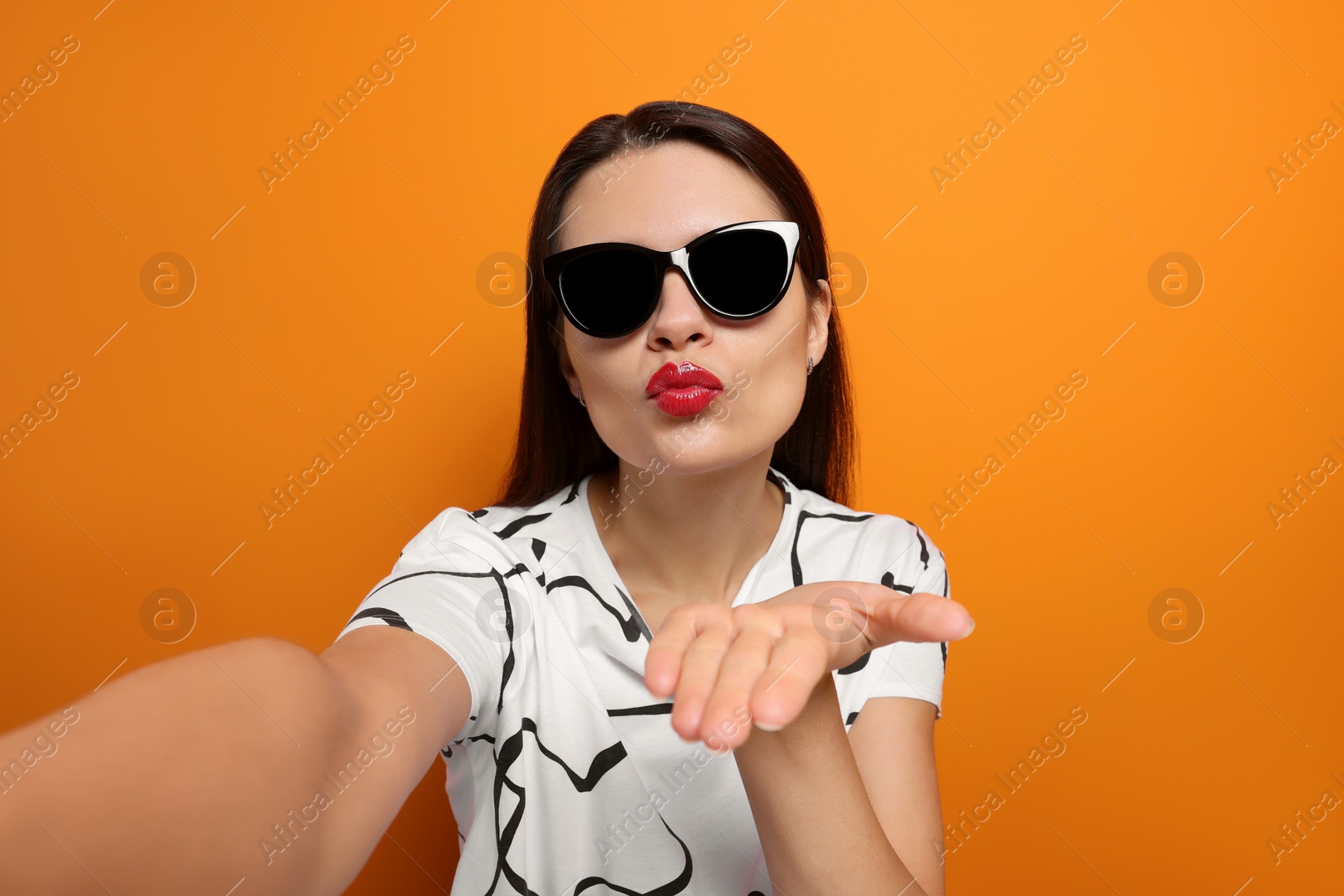 Photo of Beautiful young woman taking selfie while blowing kiss on orange background