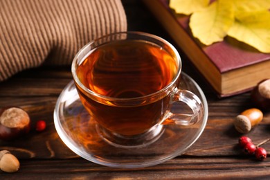 Photo of Cup of aromatic tea, book and acorns on wooden table indoors, closeup. Autumn atmosphere
