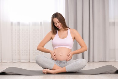 Photo of Pregnant woman sitting on yoga mat at home