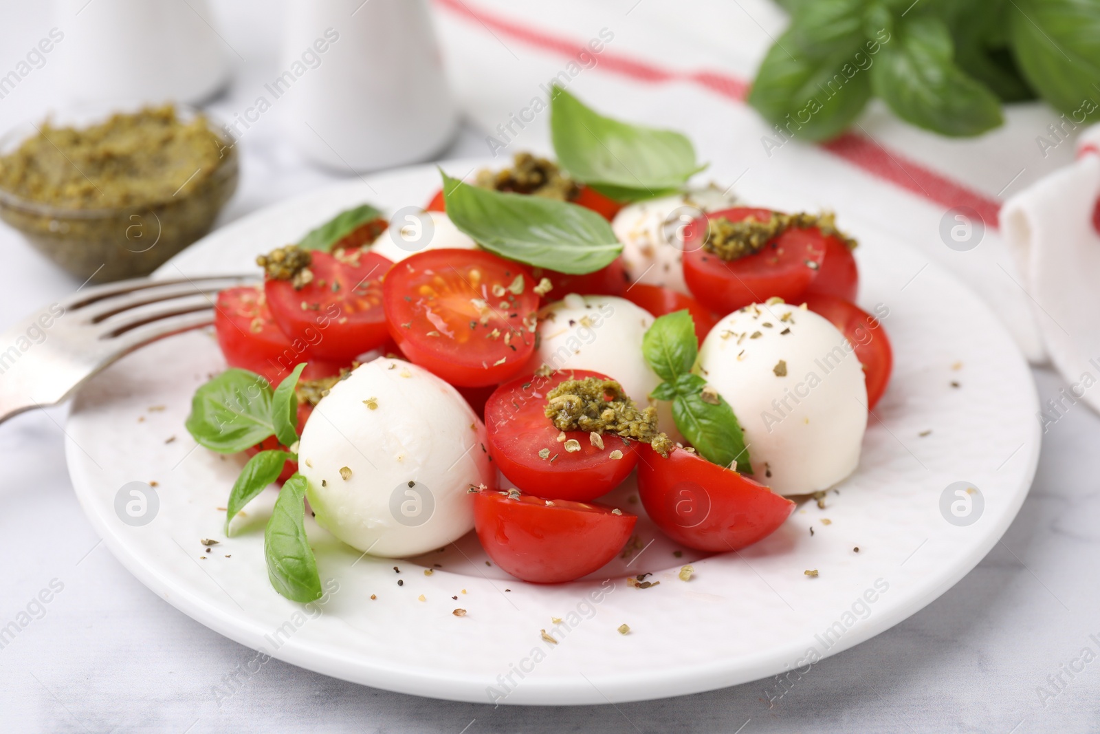 Photo of Tasty salad Caprese with tomatoes, mozzarella balls and basil on white table, closeup