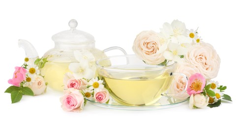 Aromatic herbal tea in glass cup, teapot and flowers isolated on white
