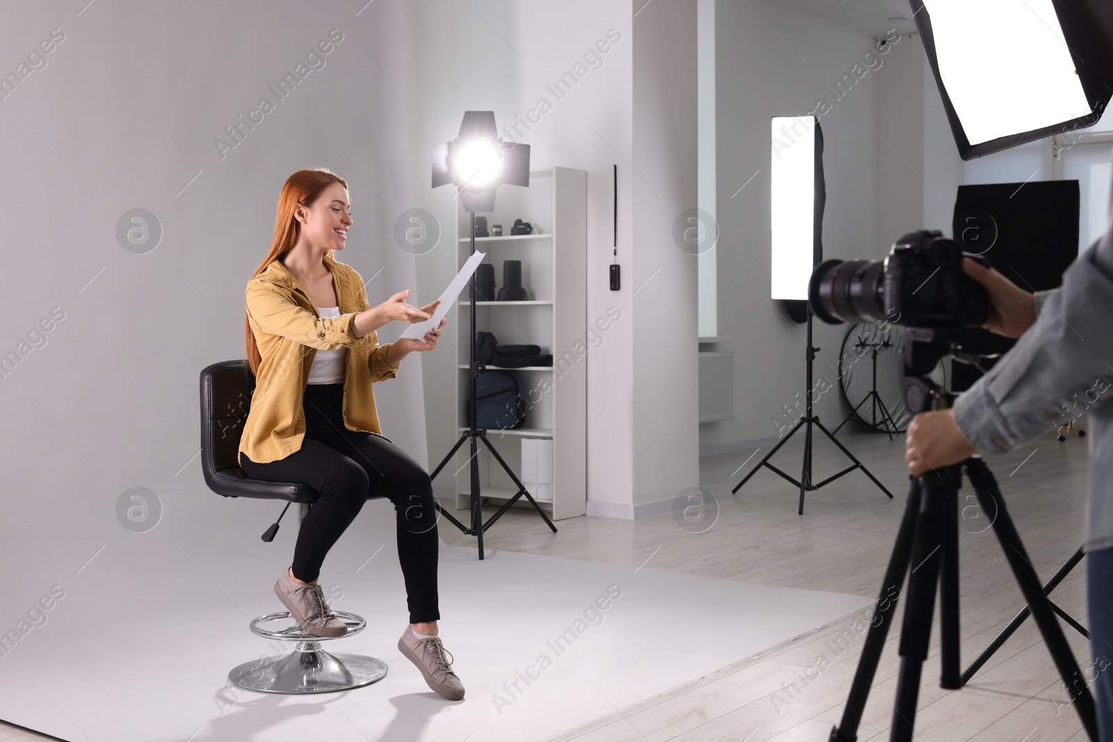 Photo of Casting call. Woman with script performing while camera operator filming her against light grey background in studio