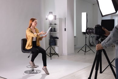 Photo of Casting call. Woman with script performing while camera operator filming her against light grey background in studio