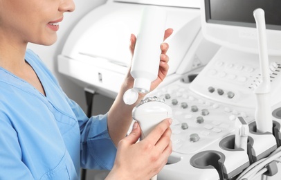 Sonographer covering ultrasound machine probe with gel in clinic, closeup