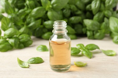 Glass bottle of basil essential oil and leaves on white wooden table